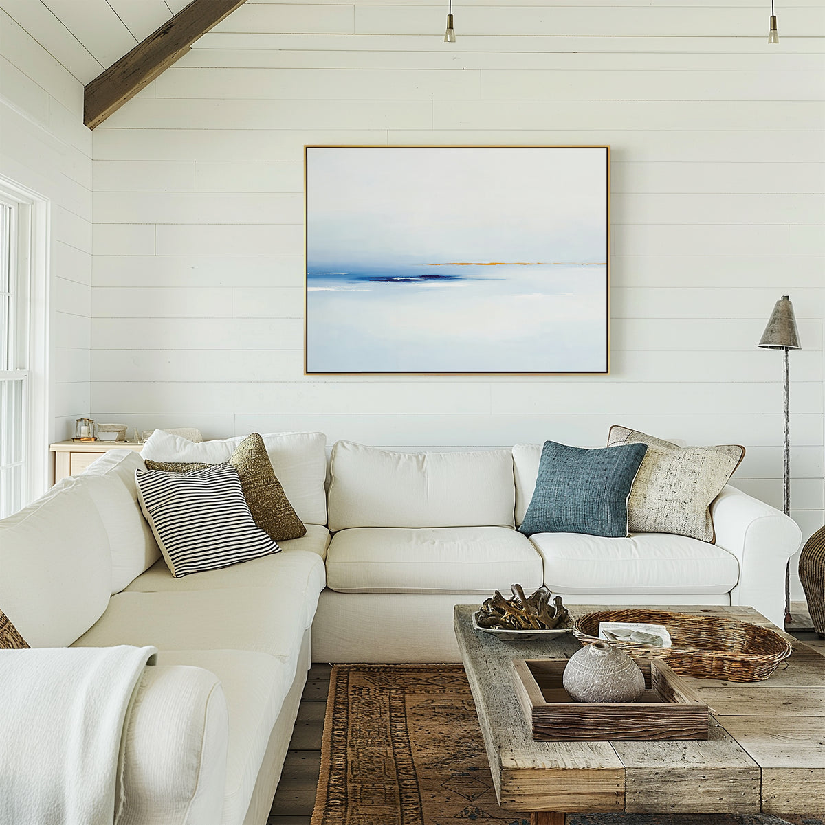 A bright, cozy living room with white shiplap walls, a large white sectional sofa with assorted throw pillows, a rustic wooden coffee table, and the Distant Archipelago Canvas Art - Horizontal hanging above the couch.
