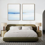 A modern bedroom featuring a green upholstered bed with white bedding, two beige nightstands with matching lamps, and the Distant Archipelago - Set Of 2 blue and white wall art above the bed for a fresh, stylish touch.