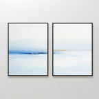 Distant Archipelago - Set Of 2 features minimalist abstract paintings in black frames with soft blue, white, and subtle orange tones, evoking a calm landscape—ideal contemporary wall art for a serene space.
