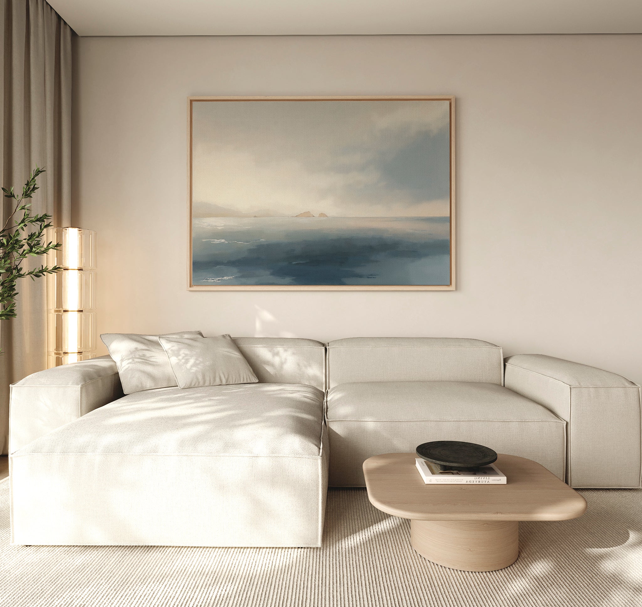 A modern living room with a light beige sectional, wooden coffee table, books, black bowl, tall plant, and the Distant Isles Canvas Art - Horizontal on a neutral wall creates a tranquil and serene home decor atmosphere.