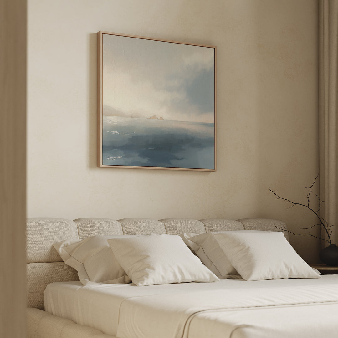 A minimal, neutral-toned bedroom features a beige upholstered bed, white bedding, and the Distant Isles Canvas Art - Square above the headboard. A simple vase with bare branches on the bedside table enhances the tranquil atmosphere.