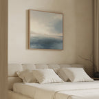 A minimal, neutral-toned bedroom features a beige upholstered bed, white bedding, and the Distant Isles Canvas Art - Square above the headboard. A simple vase with bare branches on the bedside table enhances the tranquil atmosphere.