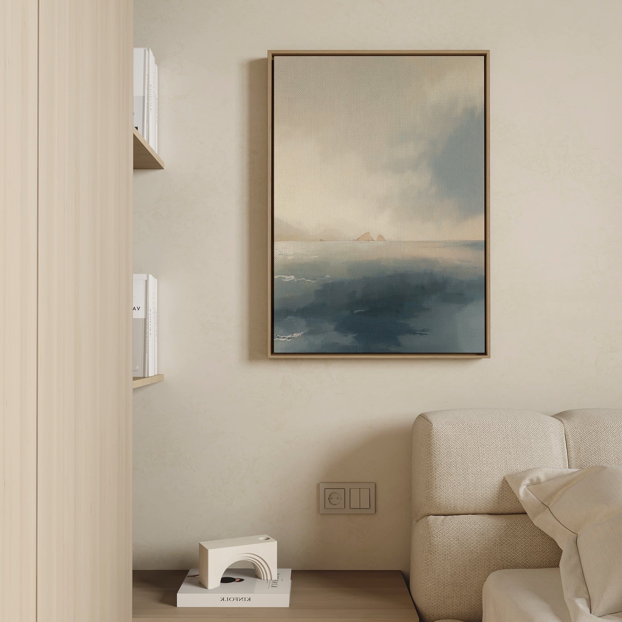 A minimalist living room corner features a beige couch, wooden shelves with white books, and the Distant Isles Canvas Art - Vertical. A small geometric sculpture on a lower shelf adds to the Nordic Park-inspired calm.