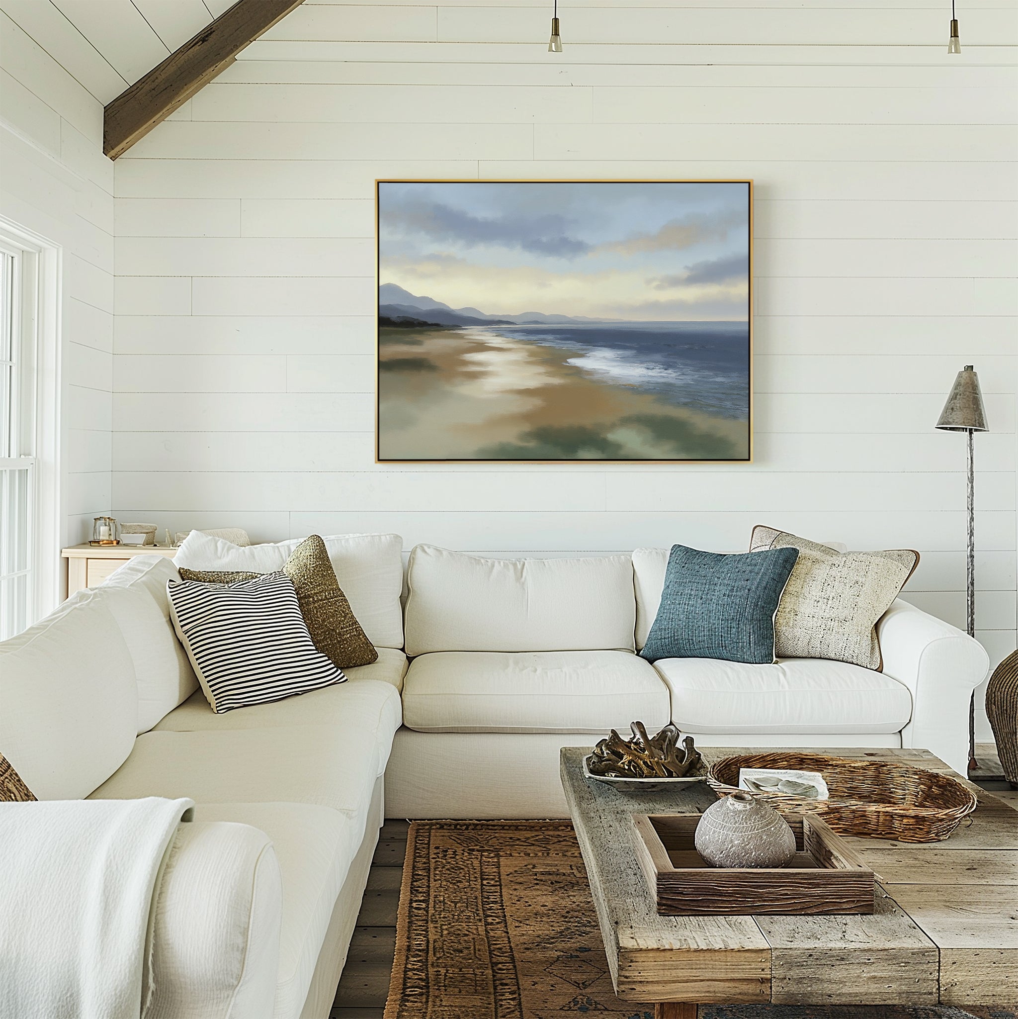 A cozy living room with a white sectional sofa, assorted pillows, a rustic wooden coffee table, and the Distant Shores Canvas Art - Horizontal depicting a tranquil beach scene on the white shiplap wall.