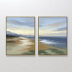 The Distant Shores - Set of 2 features framed canvas prints side by side on a white wall, each depicting tranquil mountains, a sandy shore, and a calm sea under a cloudy sunset in a peaceful coastal panorama.
