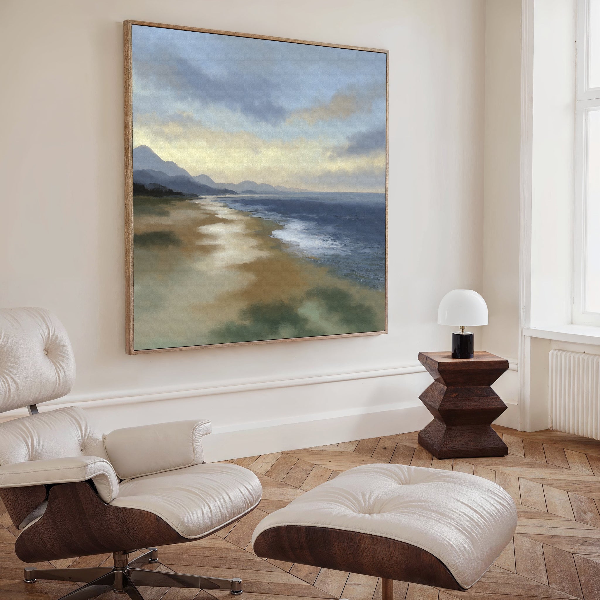 A modern minimalist living room featuring a white lounge chair and ottoman, a geometric wooden side table with lamp, and the Distant Shores Canvas Art - Square displayed on the wall.