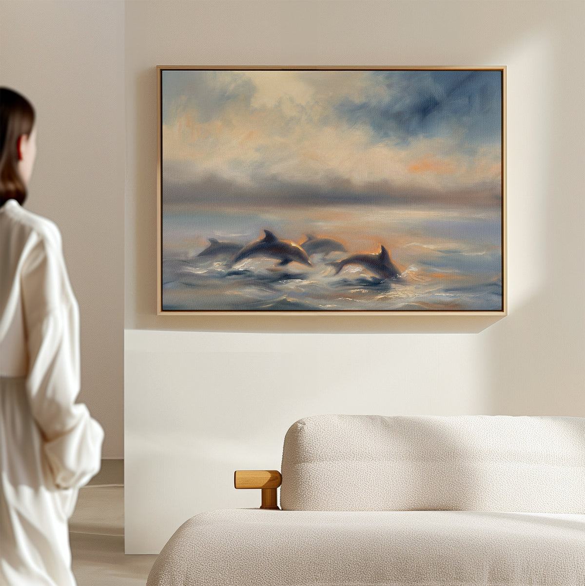 A person in a white shirt admires the "Dolphin Pod at Sunset Canvas Art - Horizontal," a large dolphin wall print hung above a cream sofa in a modern, minimalist room.