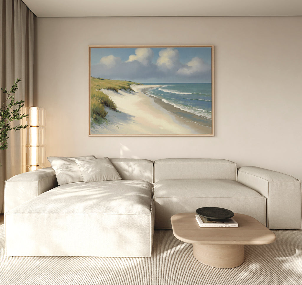 A modern living room features a light beige sectional sofa, a wooden coffee table, a potted plant, and the Dune Whispers Canvas Art - Horizontal above the sofa. Natural light fills the minimalist space, emphasizing the serene coastal artwork.