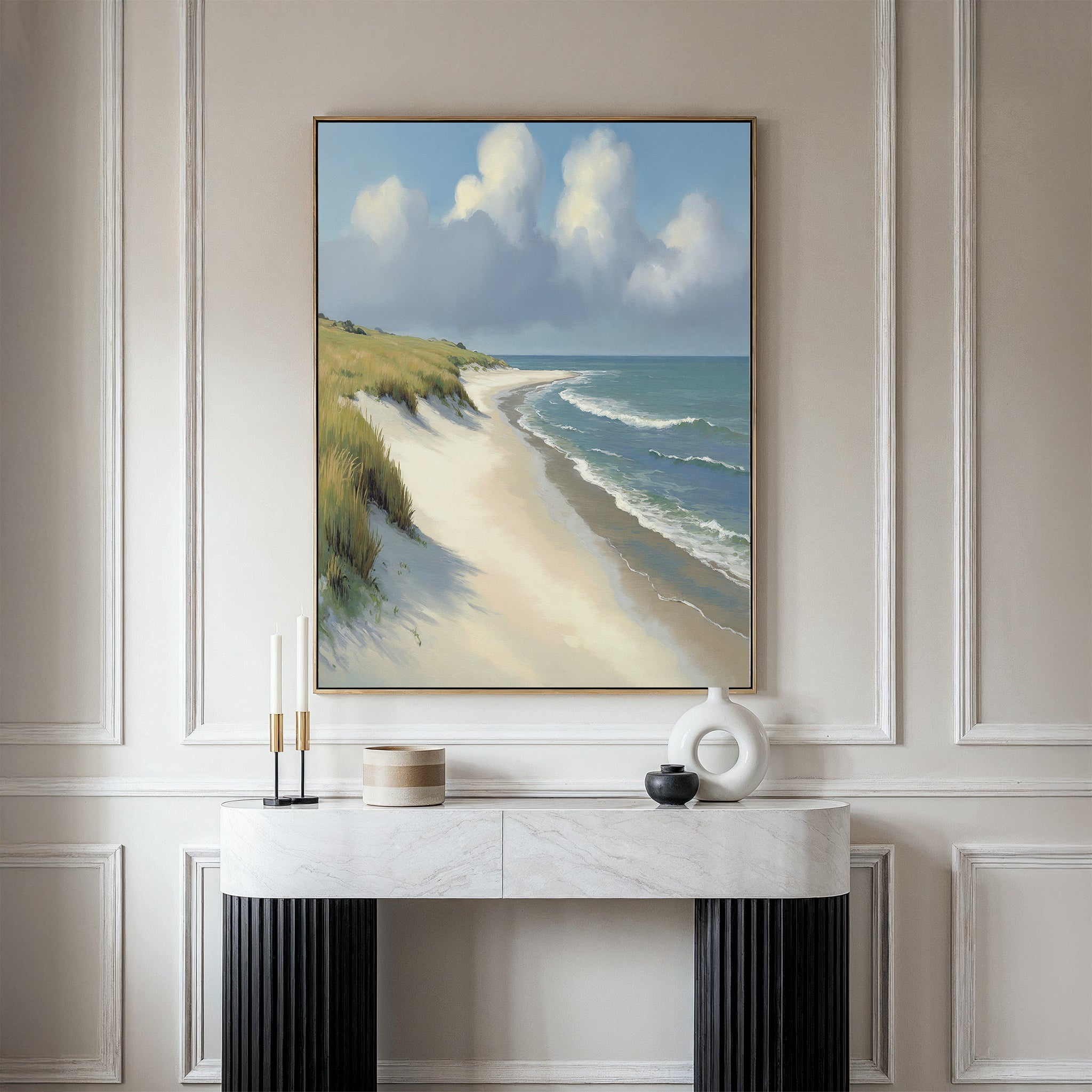 The Dune Whispers Canvas Art - Vertical, featuring a sandy beach with sea grass and waves, hangs above a marble console table adorned with modern vases and candles in a sleek, minimalist room.