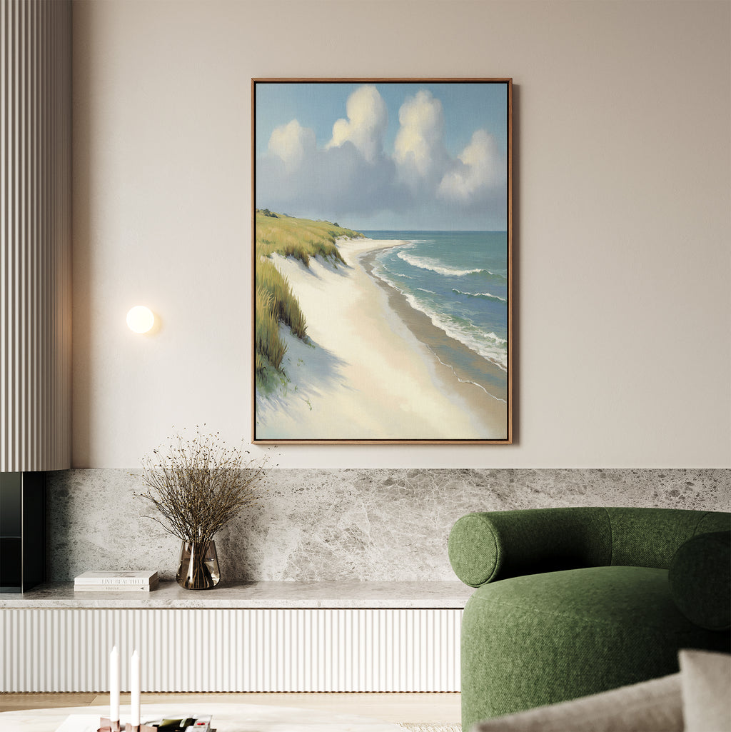 The Dune Whispers Canvas Art - Vertical, featuring sandy dunes and blue-green waves, is framed and hangs above a stone ledge in a modern living room with a green sofa and dried flowers.