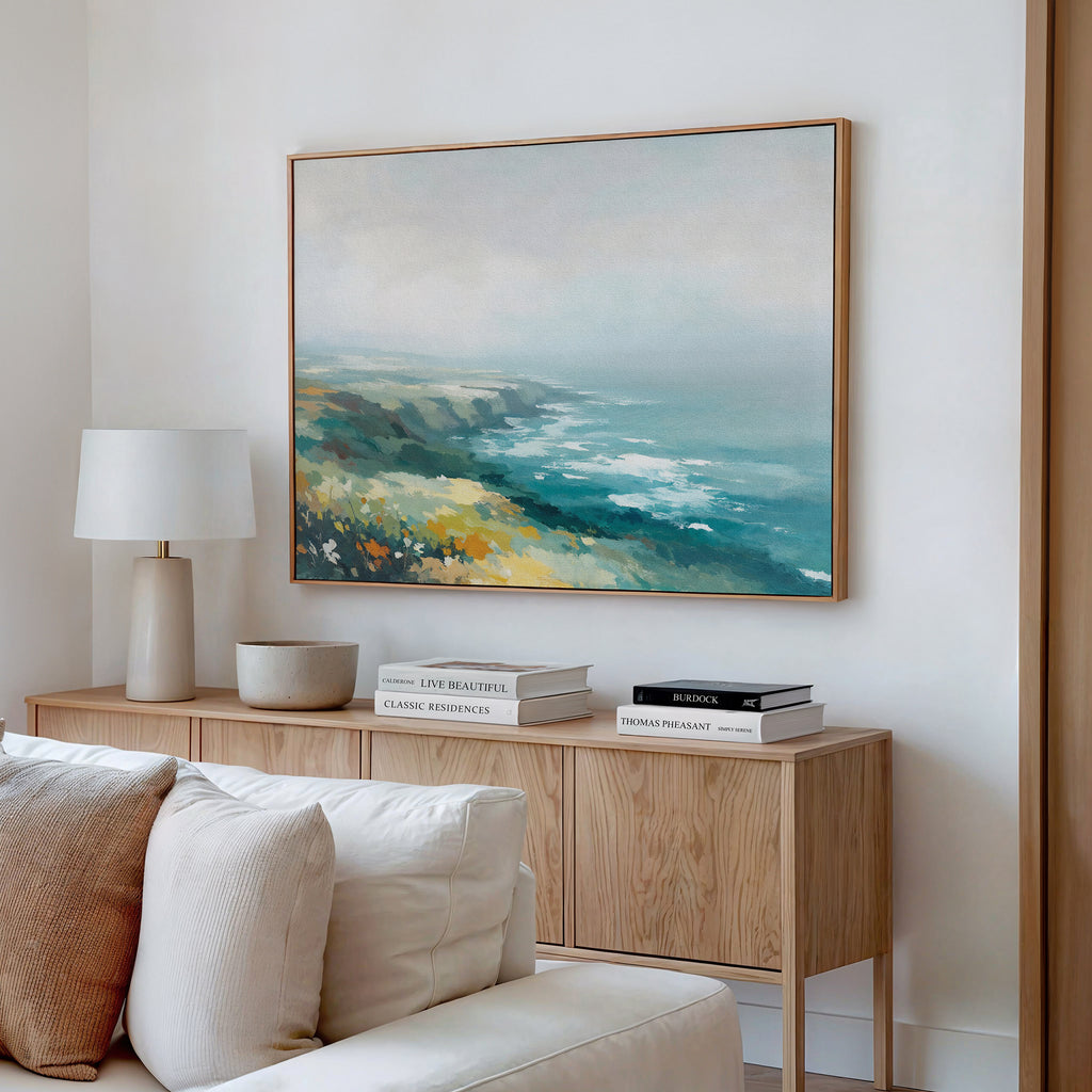 A cozy living room corner with a beige sofa, wooden sideboard displaying a lamp, bowls, books, and the Emerald Cliffs Canvas Art - Horizontal hanging above.