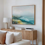 A cozy living room corner with a beige sofa, wooden sideboard displaying a lamp, bowls, books, and the Emerald Cliffs Canvas Art - Horizontal hanging above.