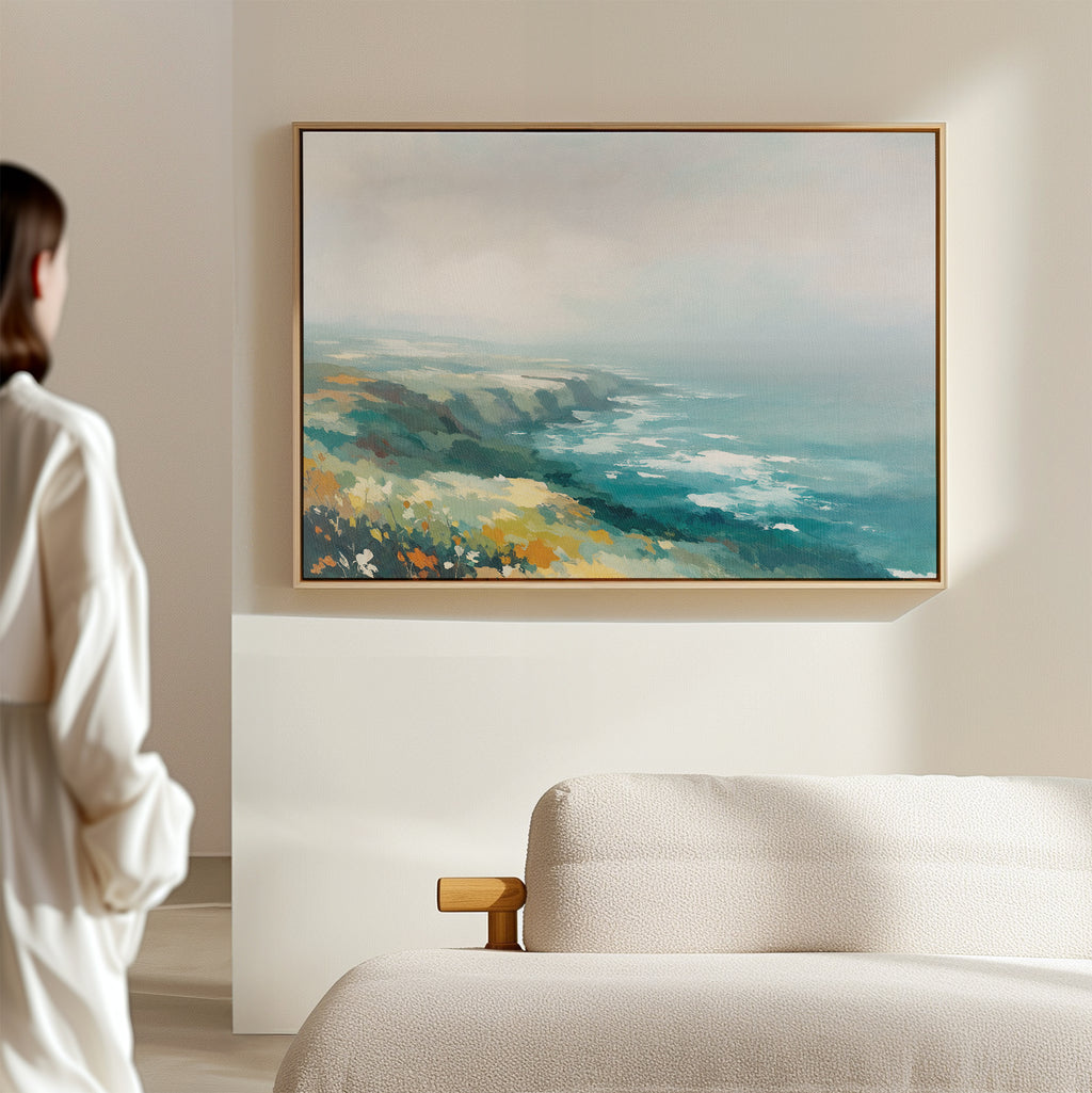 A person in a white shirt stands in a bright, minimal room, admiring the Emerald Cliffs Canvas Art - Horizontal, which hangs above a beige textured sofa.
