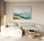 A modern living room with a light beige sectional sofa, a wooden coffee table with a black bowl, the Emerald Cliffs Canvas Art - Horizontal on the wall, a tall plant, and soft natural light streaming through floor-length curtains.