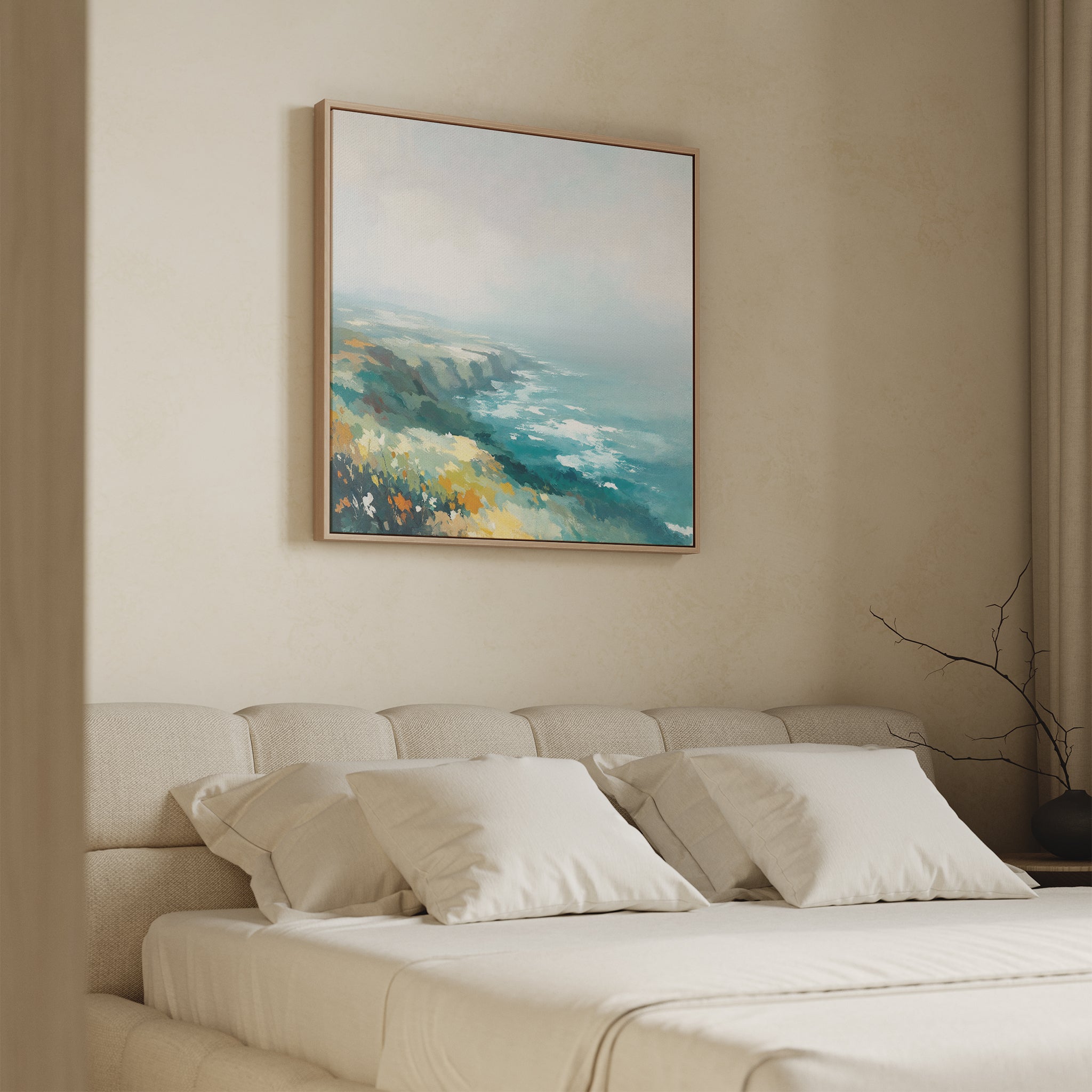 A minimal bedroom features a beige upholstered bed with white bedding and pillows. Above the bed hangs the Emerald Cliffs Canvas Art - Square, showcasing an abstract coastal landscape in blue, teal, yellow, and white.