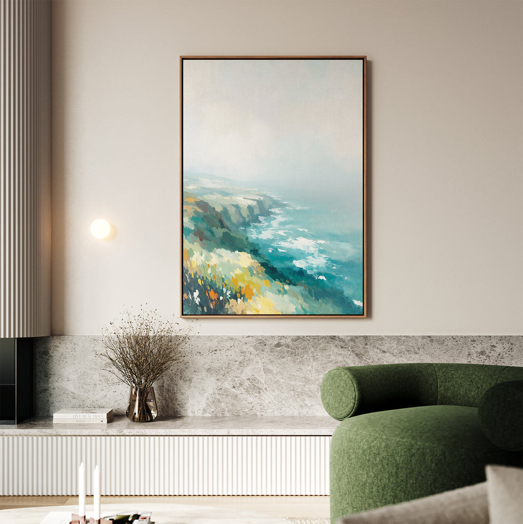 A modern living room showcases the Emerald Cliffs Canvas Art - Vertical, depicting blue water, cliffs, and yellow flowers. A green armchair, candles, and a vase with dried branches complete this serene setting.