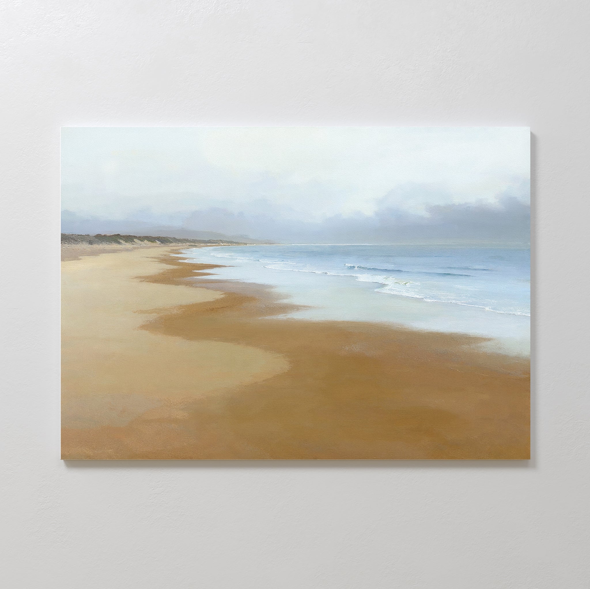 The Endless Shoreline Canvas Art - Horizontal features a calm beach with gentle waves, soft sand, and a cloudy sky on a light wall—ideal as coastal decor to create a tranquil, relaxing atmosphere in your space.