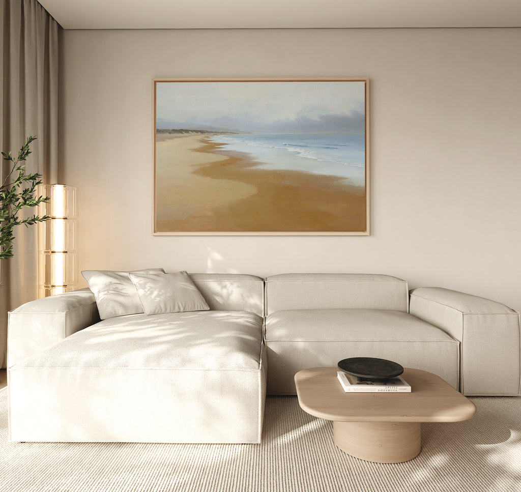 A modern living room features a light beige sectional sofa, a low wooden coffee table with a black bowl, large curtains, and the Endless Shoreline Canvas Art - Horizontal displayed above the sofa.
