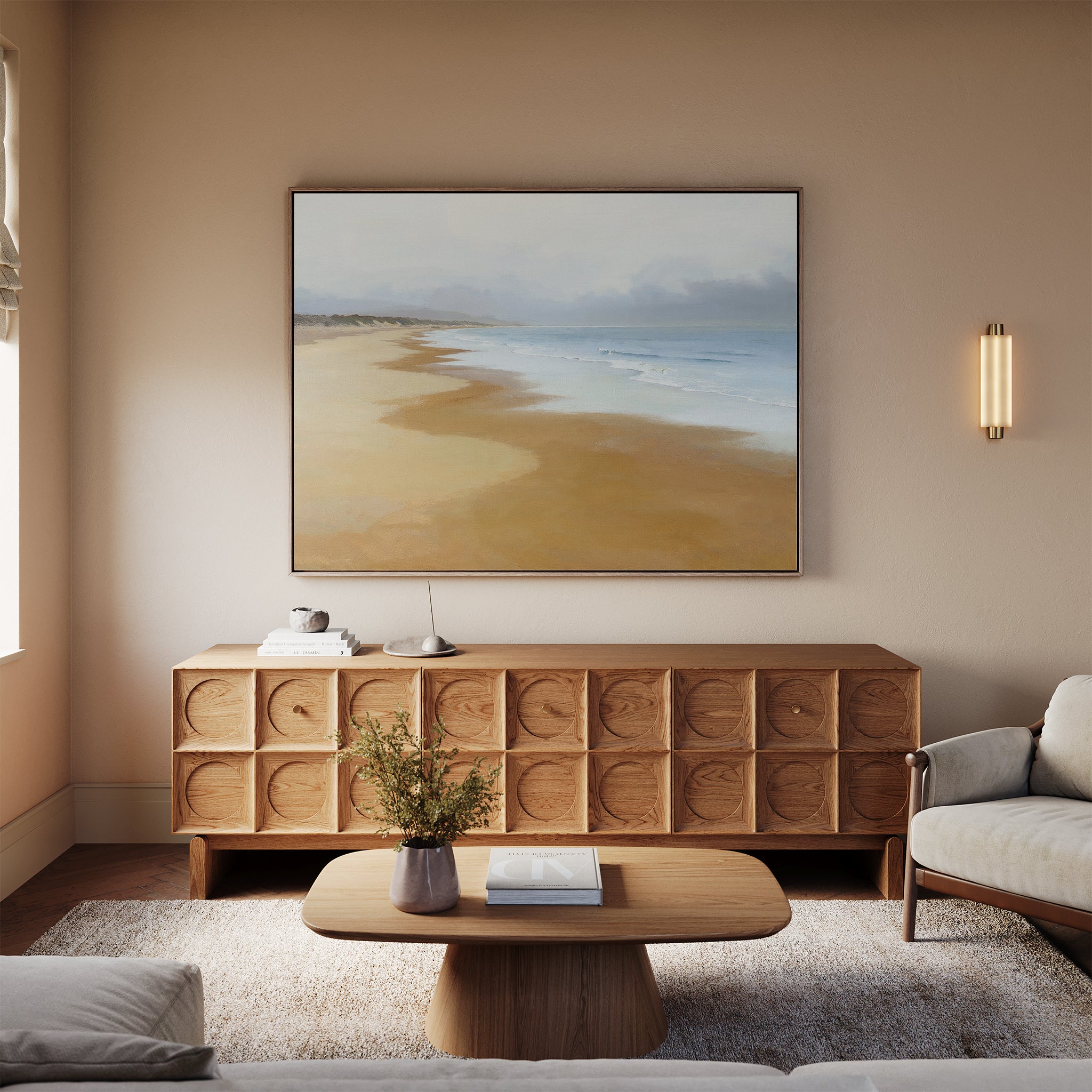 A cozy living room with a light sofa, wooden coffee table, and textured sideboard is highlighted by the Endless Shoreline Canvas Art - Horizontal above the sideboard, as natural light and decor accents enhance the inviting space.