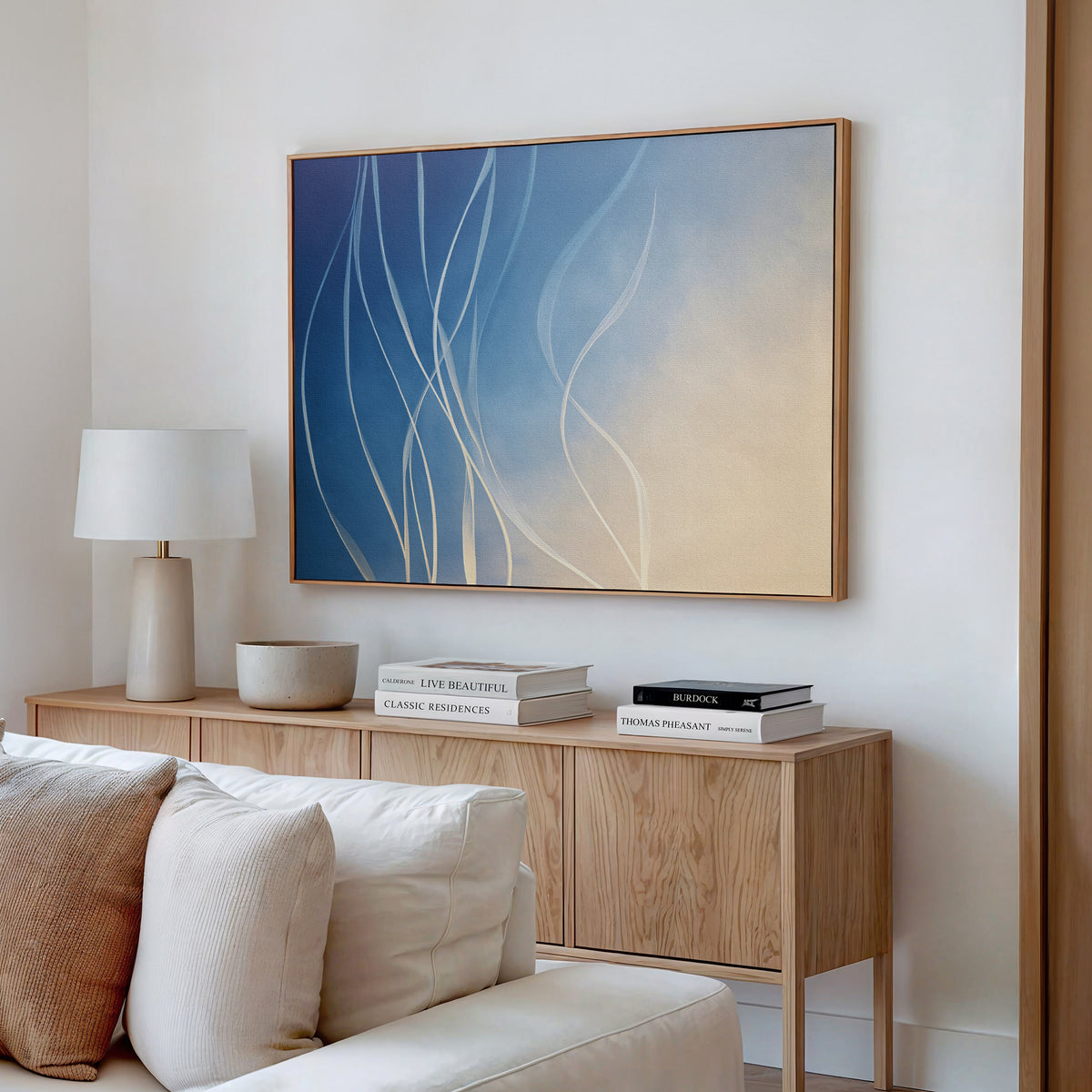 A modern living room featuring the Ethereal Lines Canvas Art - Horizontal above a cream sofa, complemented by a light wood sideboard, white books, lamp, and ceramic bowl creates an inviting Nordic Park-inspired decor.