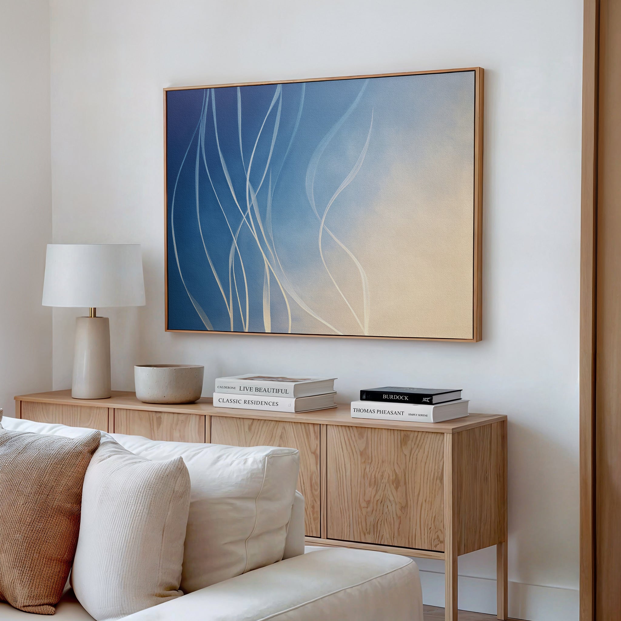 A modern living room featuring the Ethereal Lines Canvas Art - Horizontal above a cream sofa, complemented by a light wood sideboard, white books, lamp, and ceramic bowl creates an inviting Nordic Park-inspired decor.