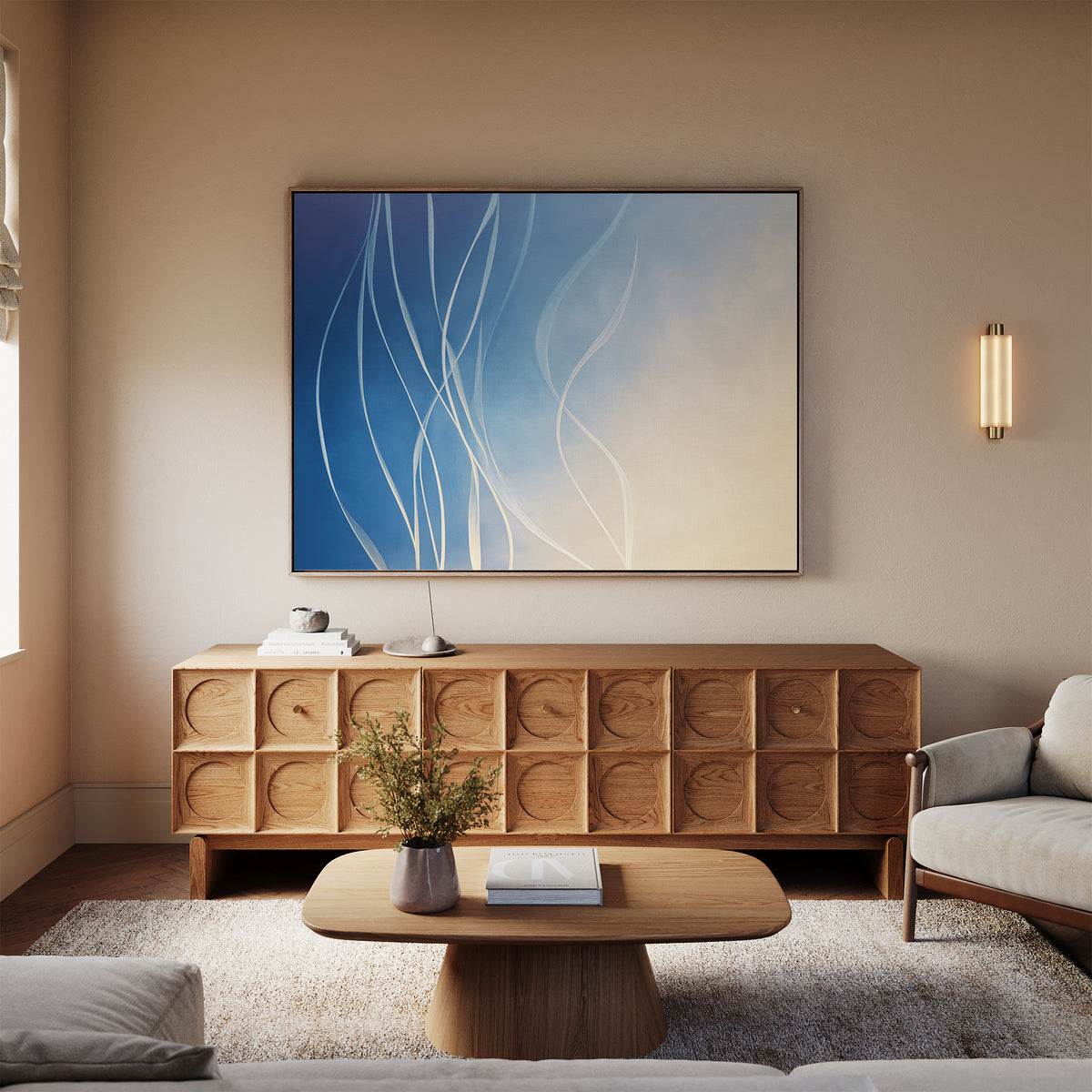 A modern living room decor with a light wood coffee table, wooden sideboard, beige sofa, neutral rug, and the Ethereal Lines Canvas Art - Horizontal in blue and white. A flower vase adds charm to this Nordic Park-inspired space.