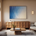 A modern living room decor with a light wood coffee table, wooden sideboard, beige sofa, neutral rug, and the Ethereal Lines Canvas Art - Horizontal in blue and white. A flower vase adds charm to this Nordic Park-inspired space.