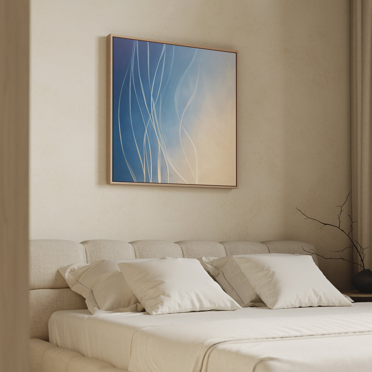 A beige bedroom features a cushioned headboard, neatly arranged pillows, and the Ethereal Lines Canvas Art - Square with blue, cream, and white lines above the bed. A bare branch in a vase on the nightstand adds charm to this serene space.