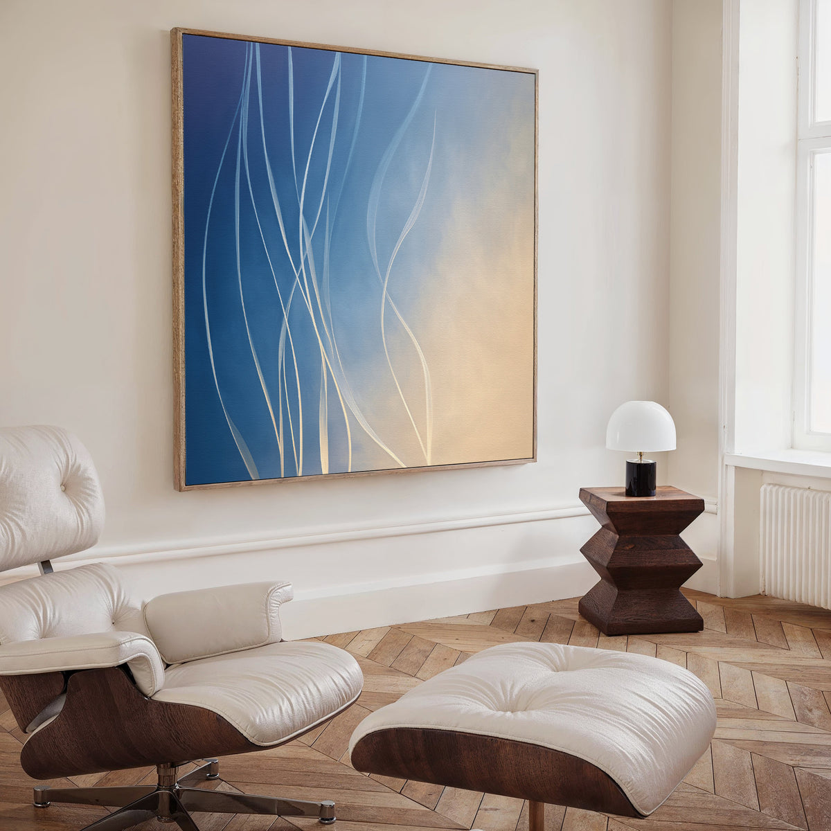 A modern living room with a white leather lounge chair and ottoman, a small wooden side table with a white lamp, and the Ethereal Lines Canvas Art - Square featuring blue and beige tones. Light streams through a tall window.