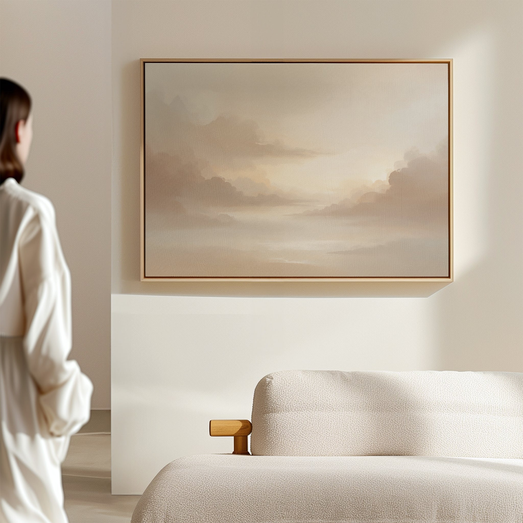 A person stands in a softly lit, minimalist room with a beige sofa and Ethereal Veil Canvas Art - Horizontal—a serene cloudy sky print—on the wall, reflecting Nordic Park’s neutral tones and tranquil atmosphere.