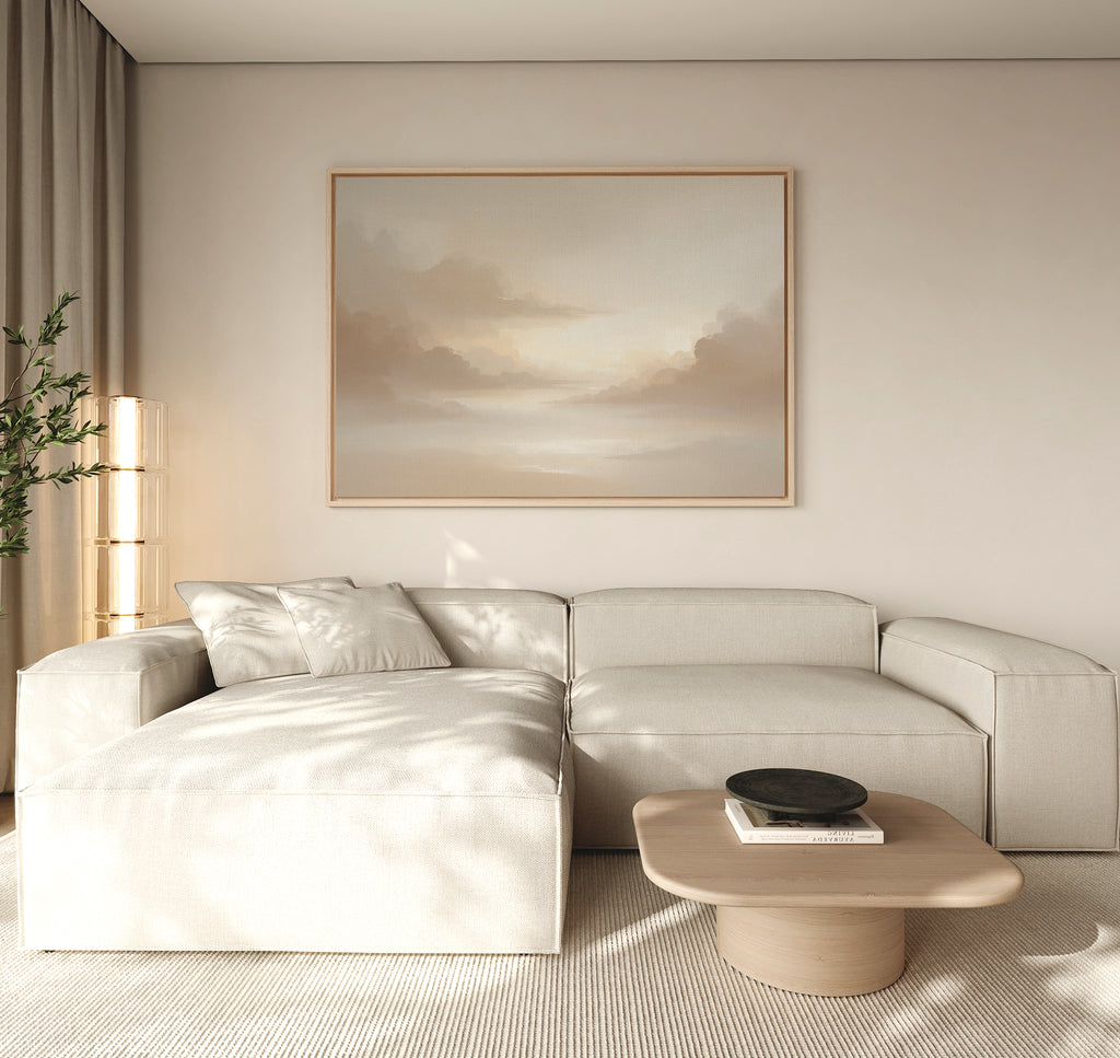 A modern living room features a light beige sectional sofa, a light wood coffee table, and the Ethereal Veil Canvas Art - Horizontal—a serene print of soft, cloudy skies. Neutral tones and gentle natural light complete the tranquil atmosphere.