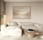 A modern living room features a light beige sectional sofa, a light wood coffee table, and the Ethereal Veil Canvas Art - Horizontal—a serene print of soft, cloudy skies. Neutral tones and gentle natural light complete the tranquil atmosphere.