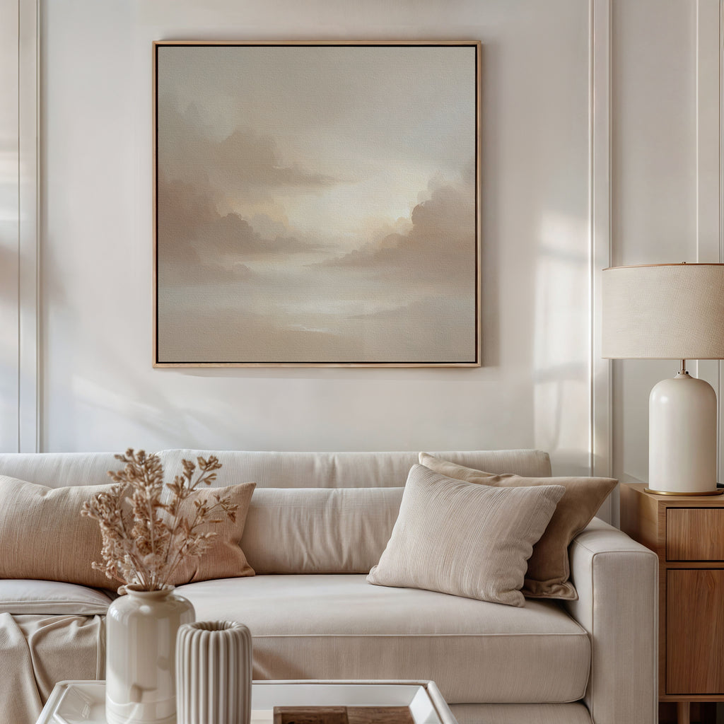 A modern living room with a beige sofa, neutral pillows, a vase of dried flowers, a table lamp, and the Ethereal Veil Canvas Art - Square featuring soft clouds above the couch. Sunlight gently illuminates the serene space.
