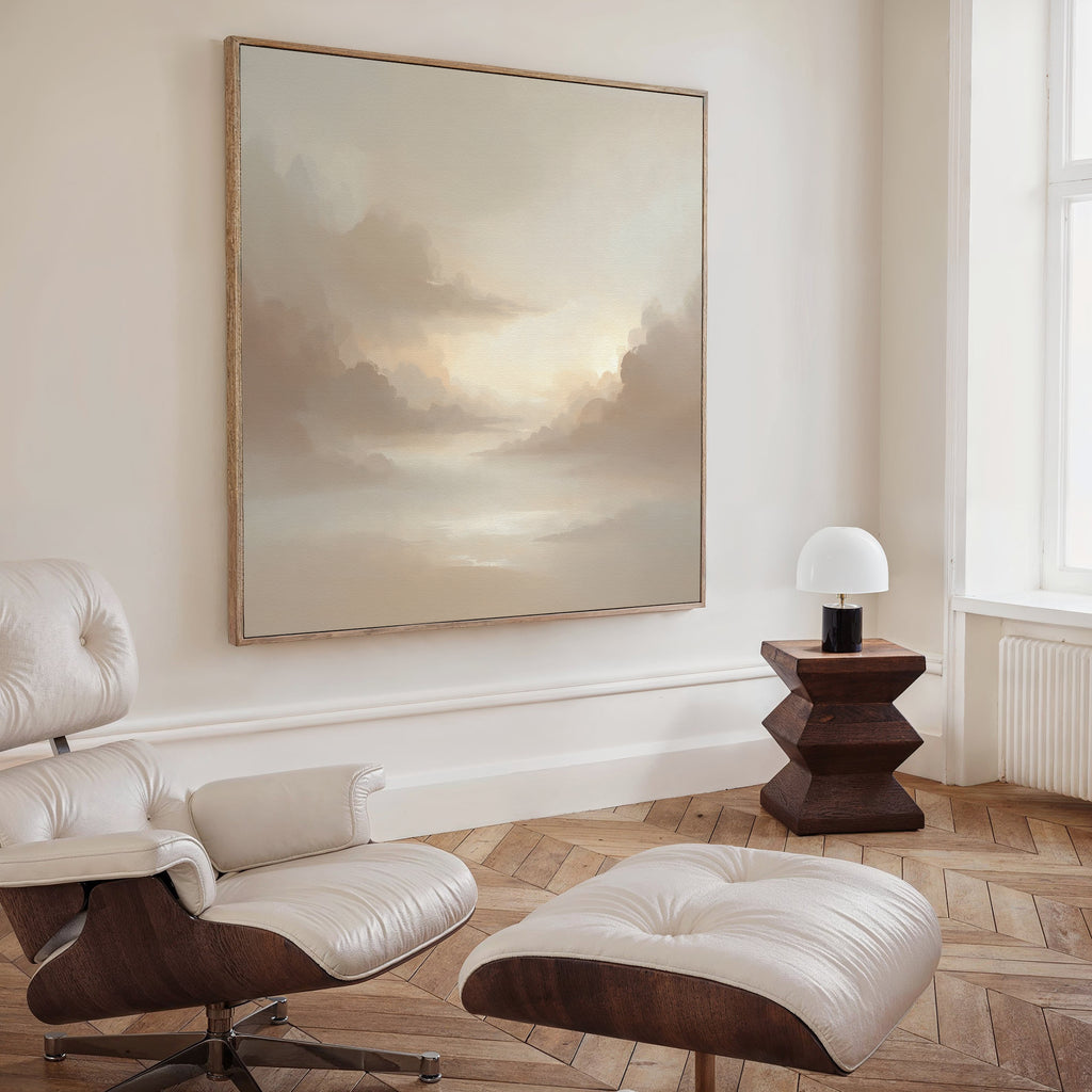 A modern, minimalist room features a white leather lounge chair and ottoman, a geometric wooden side table, and the Ethereal Veil Canvas Art - Square. Tall windows let in natural light, illuminating the soft-toned landscape on the wall.