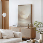 A minimal, modern living room features a cream sofa with a cushion, a wooden sideboard with ceramic vases and books, the Ethereal Veil Canvas Art - Vertical as serene wall decor, a potted plant, and a round hanging light.