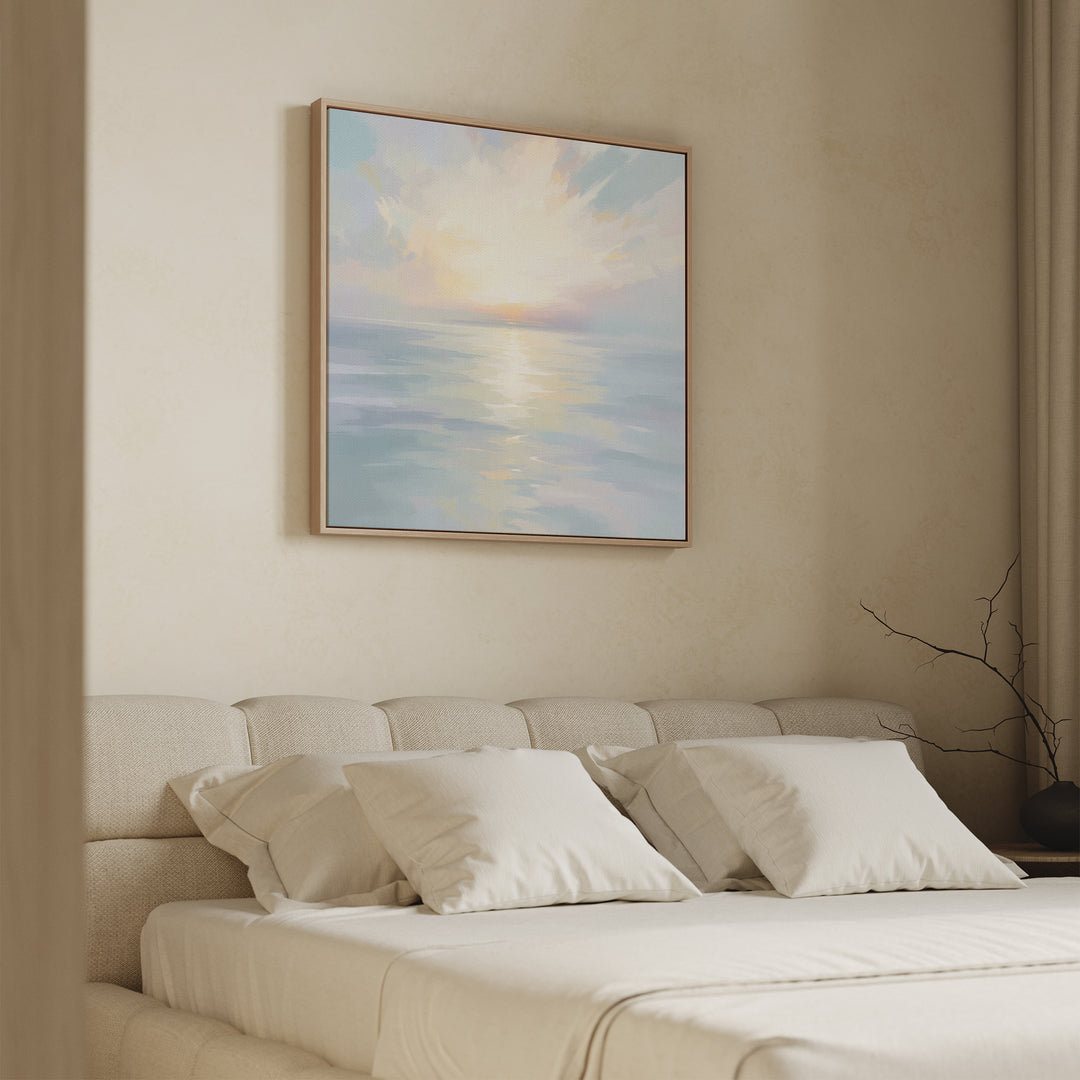 A serene bedroom features a beige bed, white pillows, and the Ethereal Waters Canvas Art - Square—a large pastel seascape—above the headboard. Natural light and minimal decor enhance the calm, peaceful atmosphere.