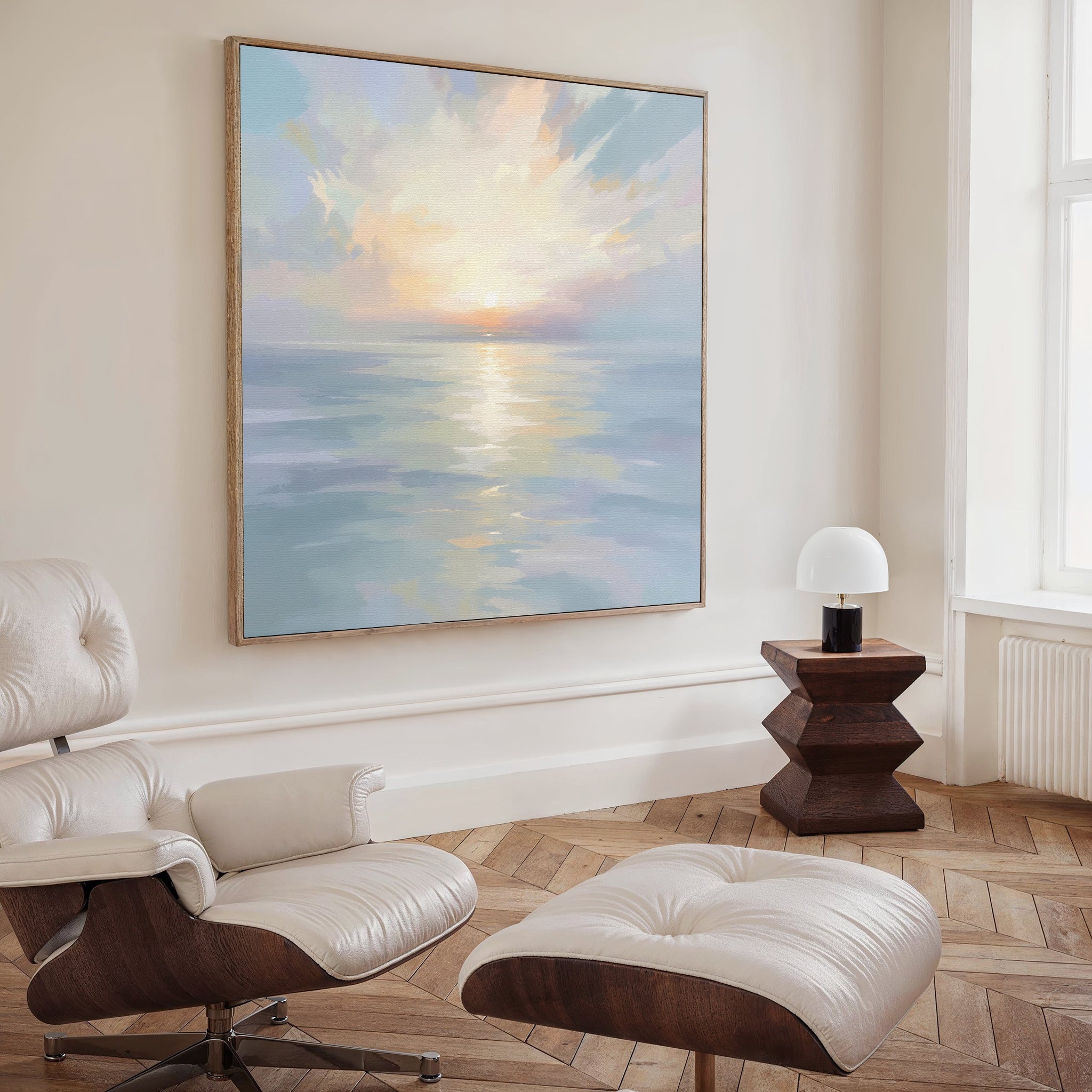 A modern living room with a white leather lounge chair and ottoman, a geometric wooden side table with a lamp, and tranquil wall art—a large Ethereal Waters Canvas Art - Square—on the wall.