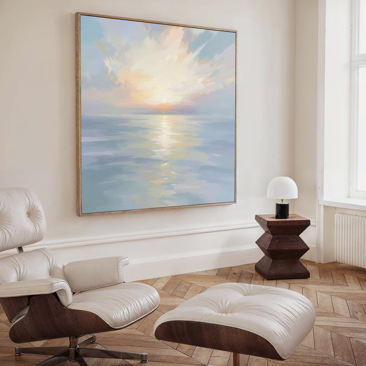 A modern living room with a white leather lounge chair and ottoman, a geometric wooden side table with a lamp, and tranquil wall art—a large Ethereal Waters Canvas Art - Square—on the wall.