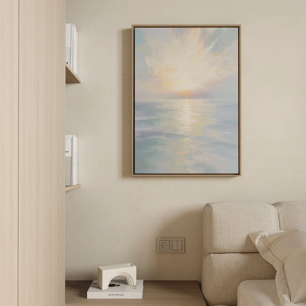 The Ethereal Waters Canvas Art - Vertical, featuring a tranquil sunrise or sunset over calm water, hangs above a light sofa in a minimalist living room with books and a white sculpture on a shelf.
