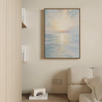 The Ethereal Waters Canvas Art - Vertical, featuring a tranquil sunrise or sunset over calm water, hangs above a light sofa in a minimalist living room with books and a white sculpture on a shelf.