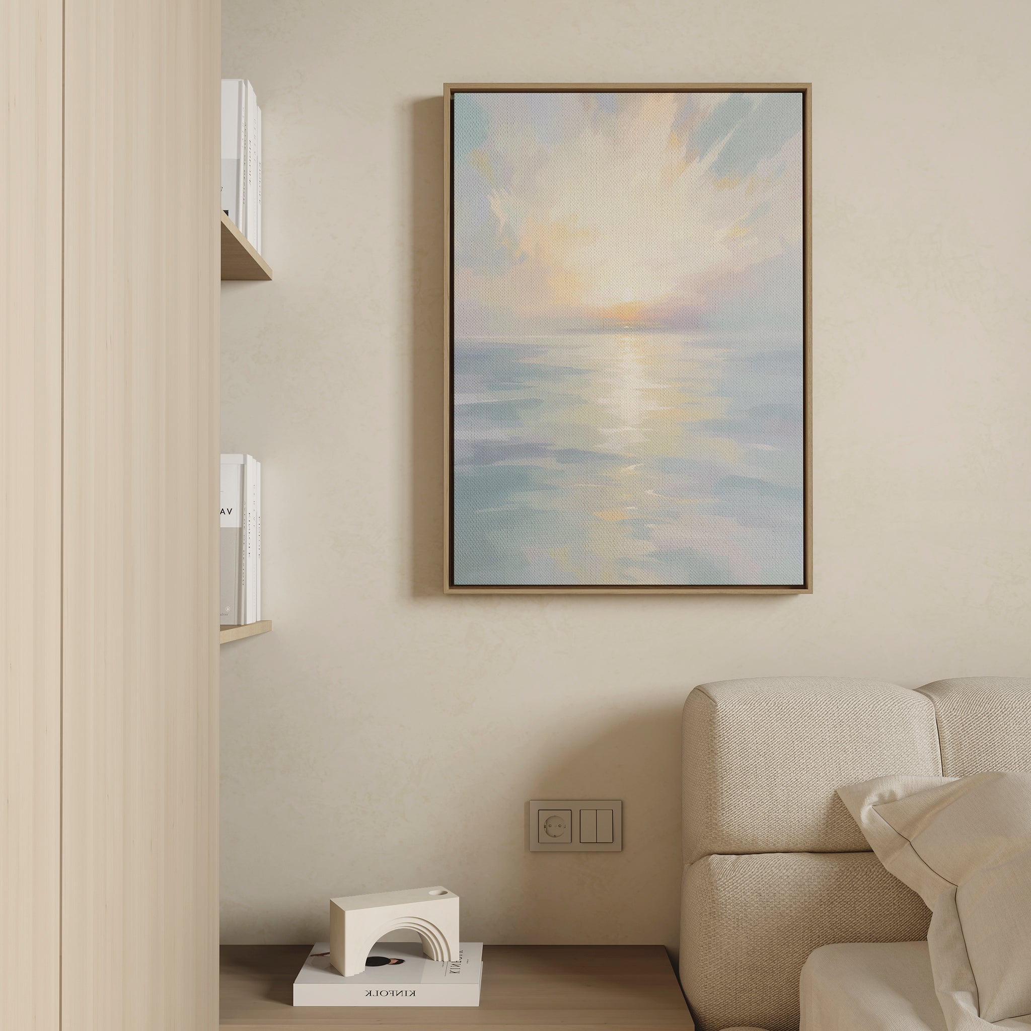 The Ethereal Waters Canvas Art - Vertical, featuring a tranquil sunrise or sunset over calm water, hangs above a light sofa in a minimalist living room with books and a white sculpture on a shelf.