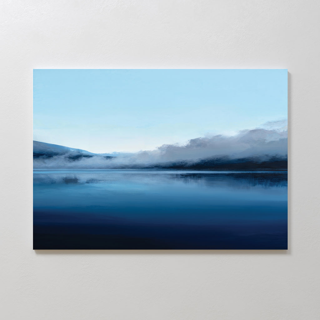 The Fjord Mist Canvas Art - Horizontal features a serene landscape of a calm lake, blue skies, misty mountains, and low clouds—creating a tranquil home decor accent for any space.