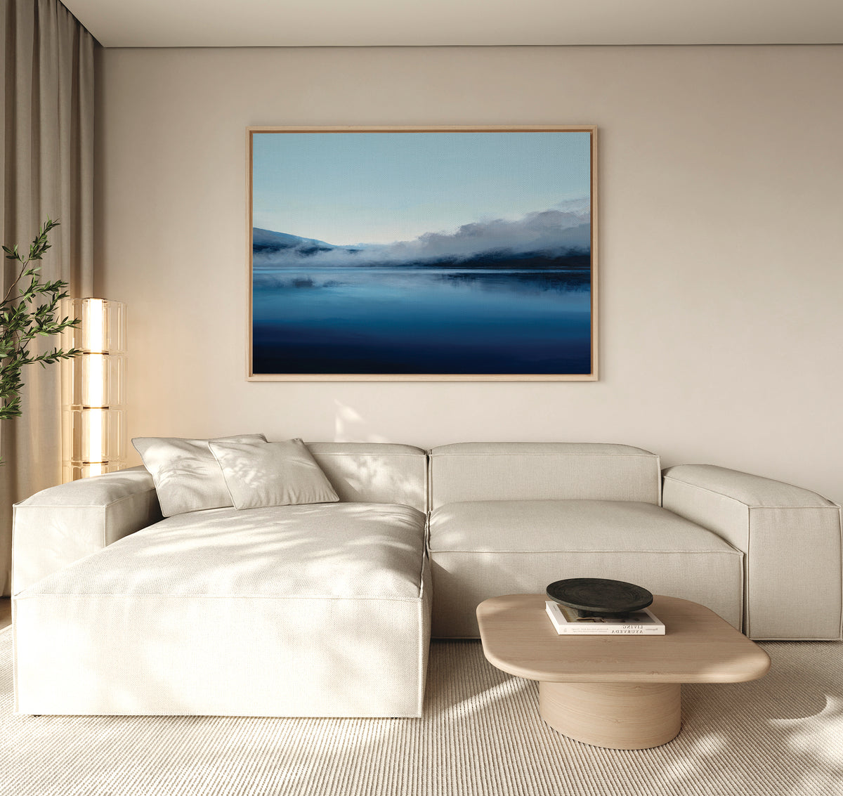 Minimalist living room with a light beige sectional sofa, wooden coffee table, and the Fjord Mist Canvas Art - Horizontal depicting serene blue mountains and water. A tall plant and sheer curtains complete this tranquil decor.