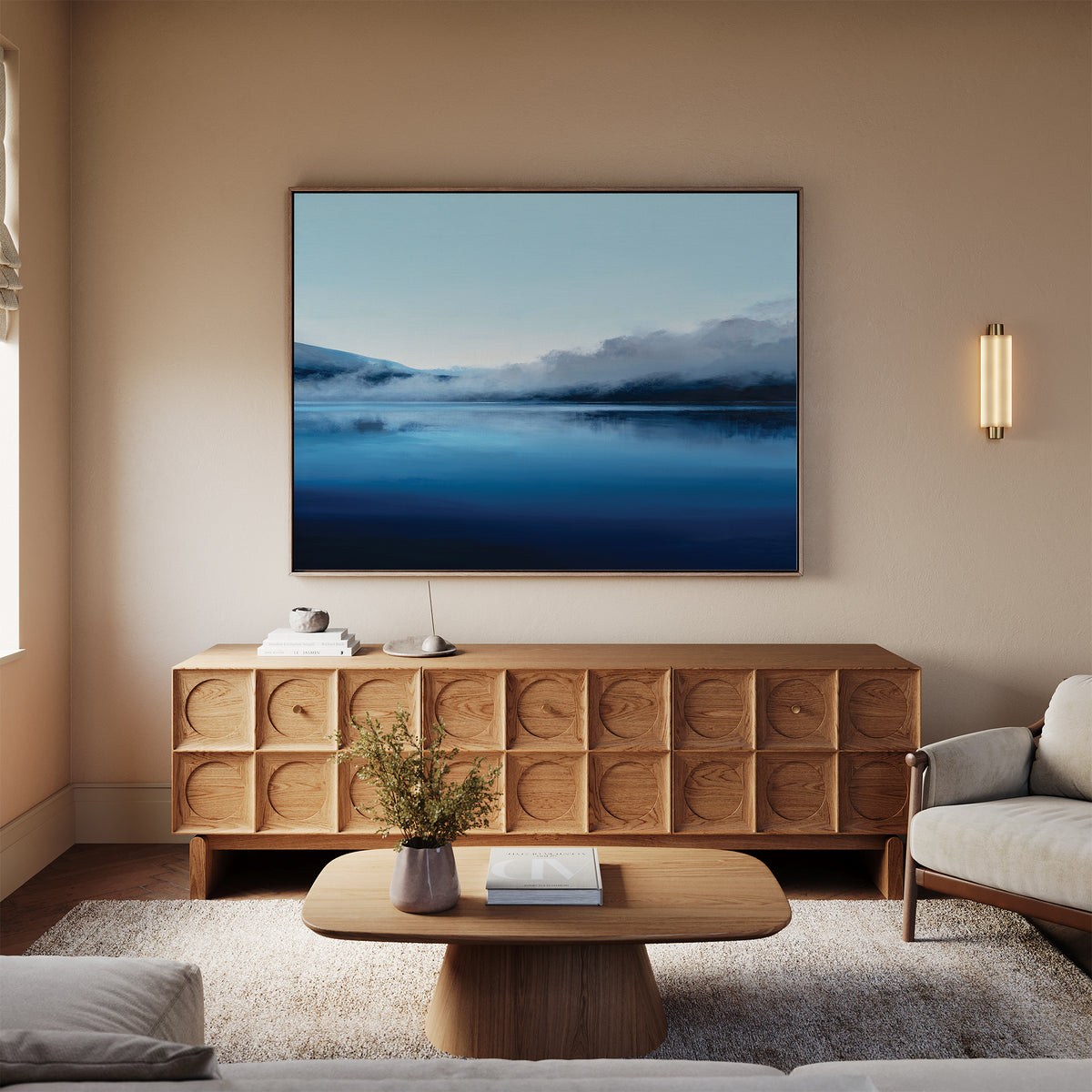 A cozy living room with a beige sofa, wooden coffee table, and a sideboard with circular patterns. Above the sideboard, the Fjord Mist Canvas Art - Horizontal brings serene Nordic landscape vibes to the decor.