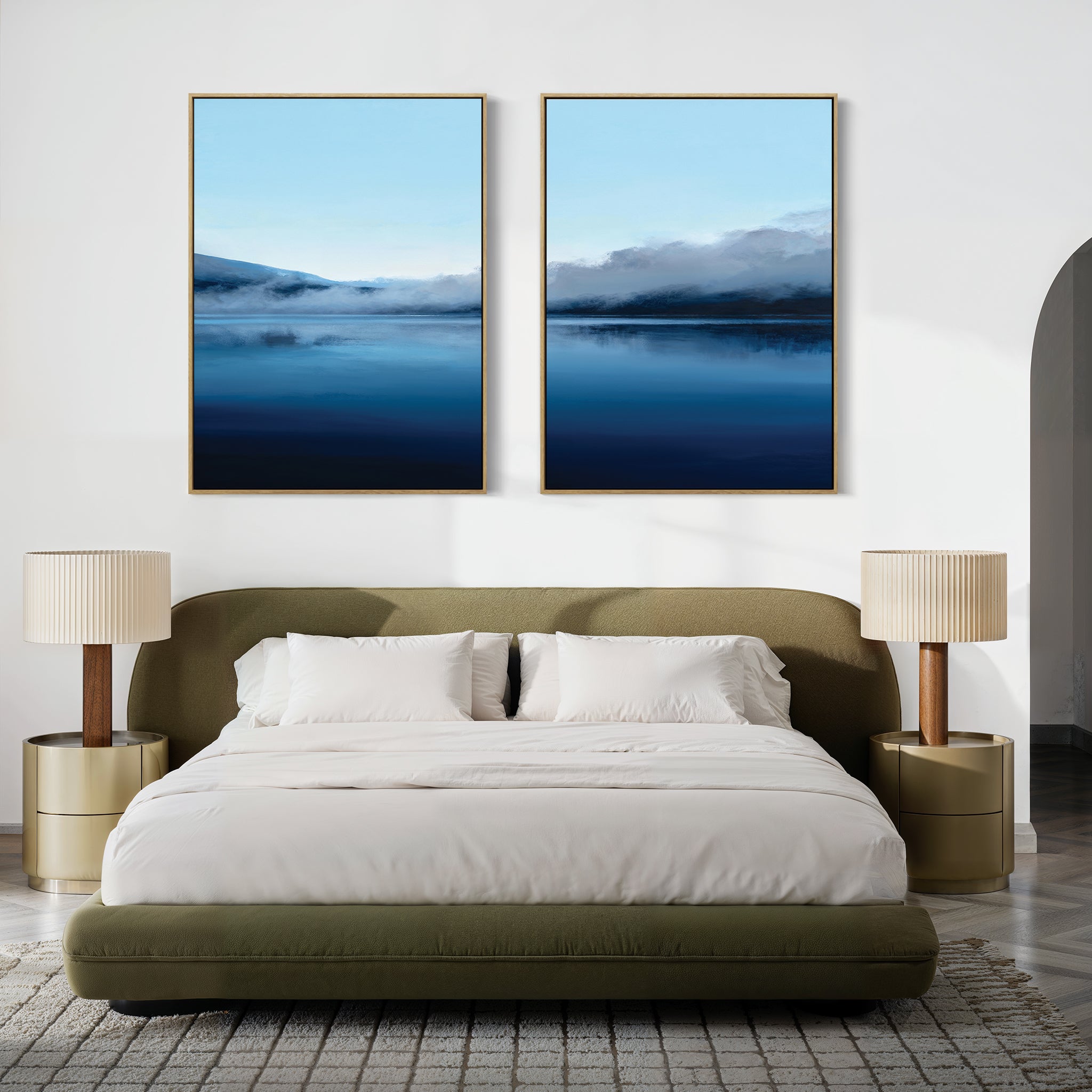 A modern bedroom featuring an olive-green bed, neutral bedding, two gold nightstands with beige lamps, and the "Fjord Mist - Set Of 2" blue artwork above the bed. A light rug covers the floor.