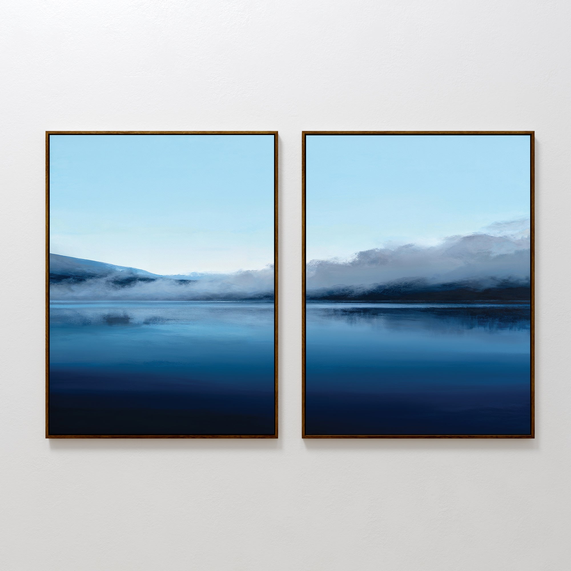The Fjord Mist - Set Of 2 features framed prints of serene landscapes with misty mountains and reflections on calm blue waters, displayed side by side on a white wall under a pale sky.