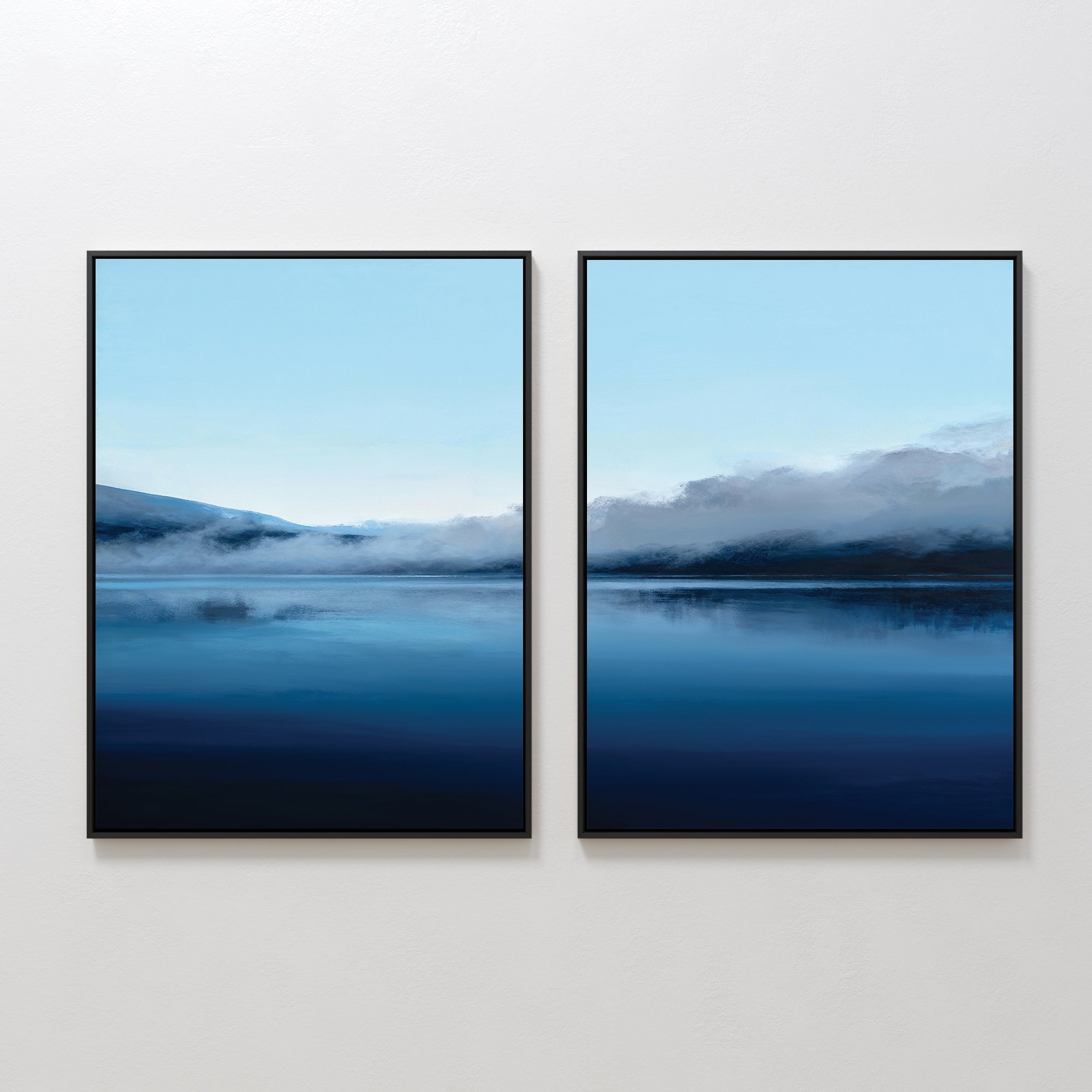 The "Fjord Mist - Set Of 2" features two framed landscape prints with misty mountains and calm blue waters. Inspired by Nordic Park, the blue and white tones evoke a serene and tranquil ambiance.