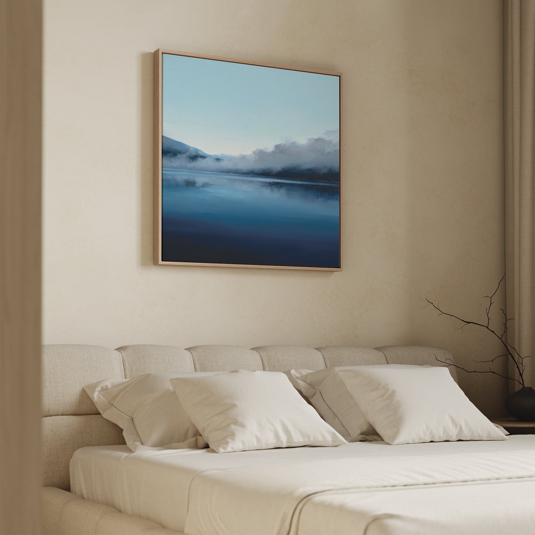 A neatly made bed with white pillows and bedding sits beneath the Fjord Mist Canvas Art - Square, featuring a serene misty lake and mountains, adding tranquility to the minimalist bedroom decor. A bare branch decorates a nearby table.