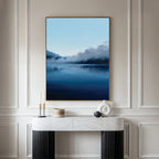 A modern living space with a white marble console table, black legs, and minimalist Nordic decor, featuring the Fjord Mist Canvas Art - Vertical—a large serene landscape of a blue lake with misty mountains above the console.
