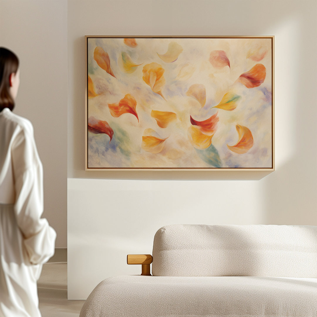 A person in a white robe admires the Floating Petals Canvas Art - Horizontal, featuring vibrant petals above a beige sofa in a modern, softly lit living room.